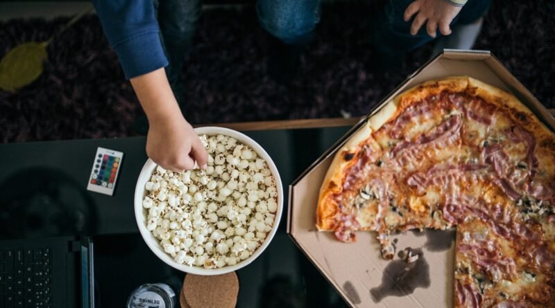 Family members gather in a cozy living room, sharing a large pizza and a bowl of popcorn while enjoying their favorite movie together, creating cheris