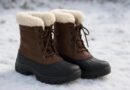 Par de botas marrons com forro claro e biqueiras pretas apoiadas na neve.
